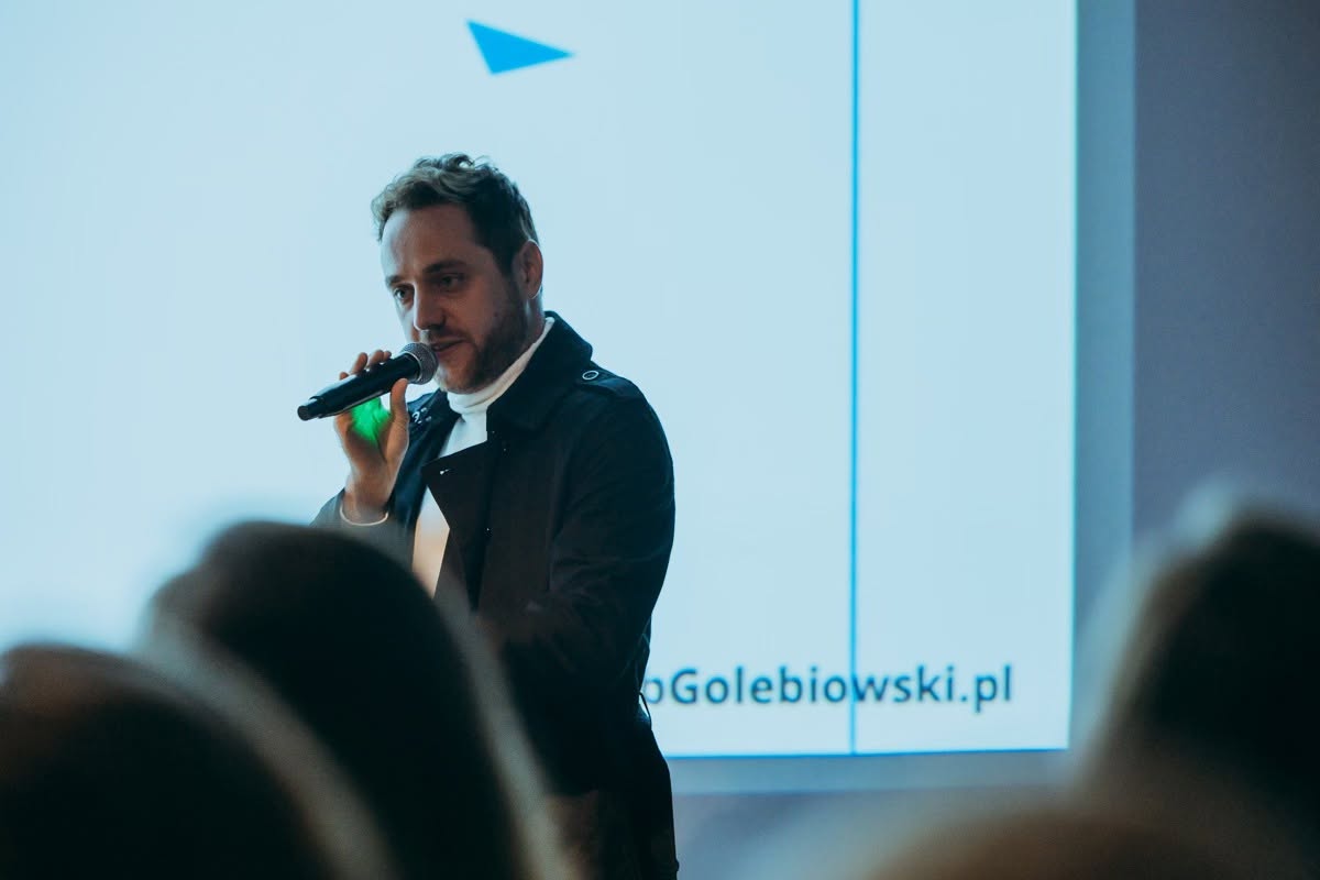 Jakub Gołębiowski występujący przed publicznością na tle ekranu prezentacji